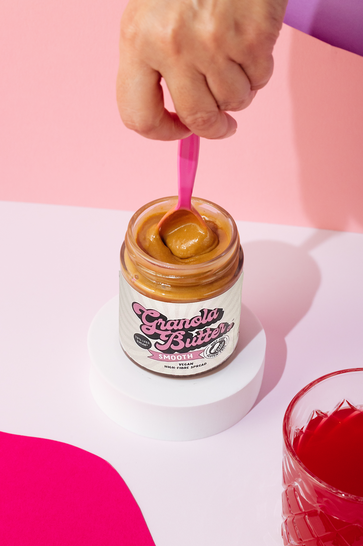A pink spoon swirling the gluten free and high fibre smooth granola butter in the jar.